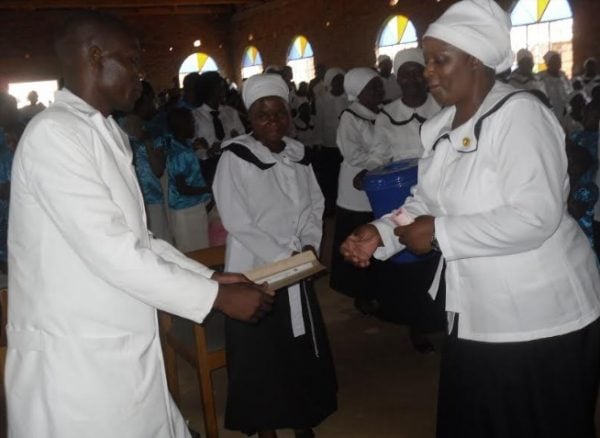 Mwangonde (c) presents cheque to evangelist Phiri as other church members sing and Mdooka in reddish rob congratulates Phiri in white robe. 