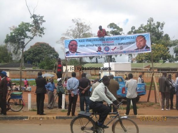 DPP diehard Lifa Andrew crimbs top to maintain the bill-board near Mzuzu Health centre as some members witness