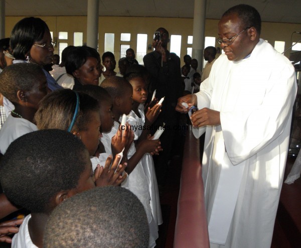 Father Benito Masuwa administering a religious rite on children in church