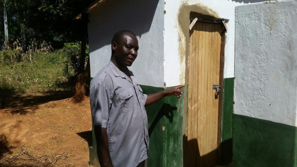 Kafumbata stands in front of one of the sanitary facilities built by Gewe project.