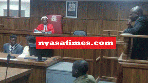 Manganya (R) stands in the dock as he listens to the judge in Cashgate episode