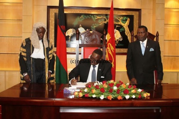 President ProffPeter Mutharika signs the visitors book at Parliament while the Soeaker Richard Msowoya and DPP MP George Chaponda looks on pic by Lisa Vintulla.