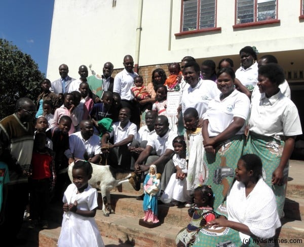 Some members of St Don Bosco posing for a group photo with their trophy, live goat and certificate at the main entrance of St Pius Parish Church. On the far left (in glasses) is Parish Priest Father Benito Masuwa.